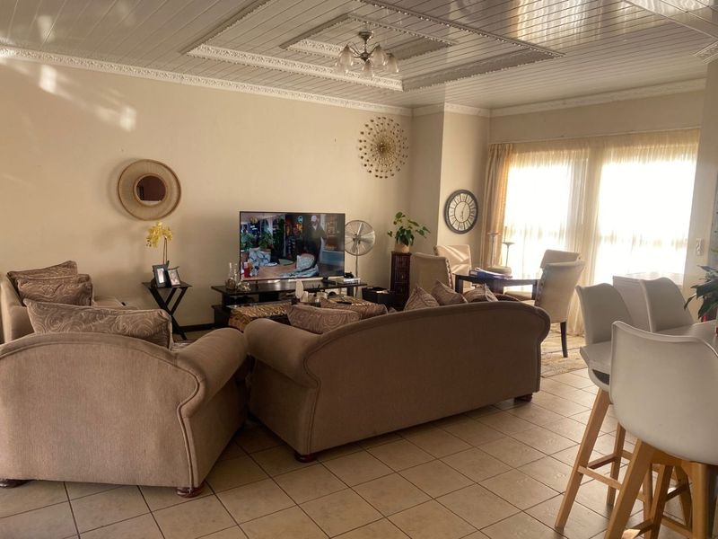 Spacious open-plan living area featuring tiled flooring and a decorative coffered ceiling with ample natural light from large windows.