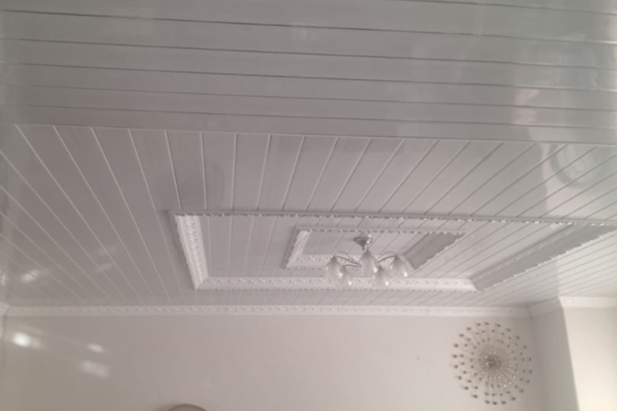 A view of a living room interior featuring white PVC panelled ceilings with decorative coving and a central light fixture.