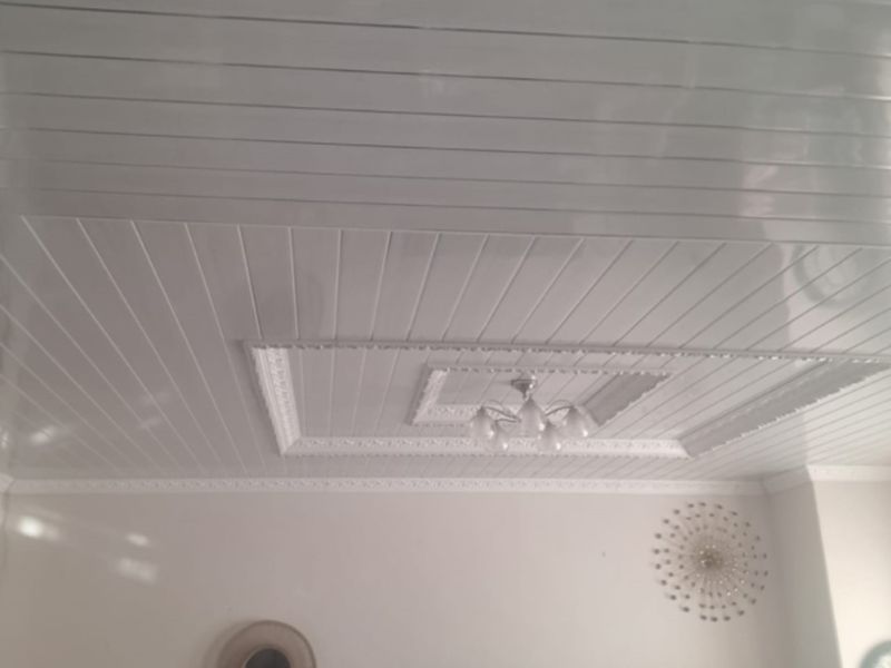 A view of a living room interior featuring white PVC panelled ceilings with decorative coving and a central light fixture.