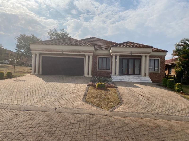 Front elevation of a single-story brick house featuring a double garage, paved driveway, and a covered entrance with decorative columns.