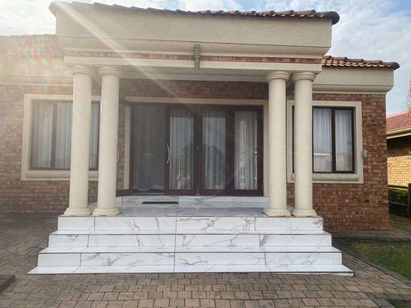 Front entrance featuring a covered porch with classical columns, marble-look tiled steps, and brick facade construction.