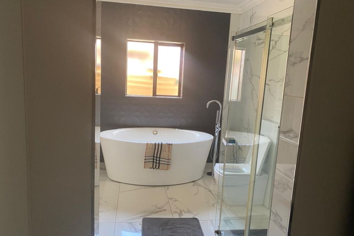 Modern bathroom featuring a sleek freestanding bathtub, glass-enclosed shower, and elegant marble-look tiling with a dark textured feature wall.