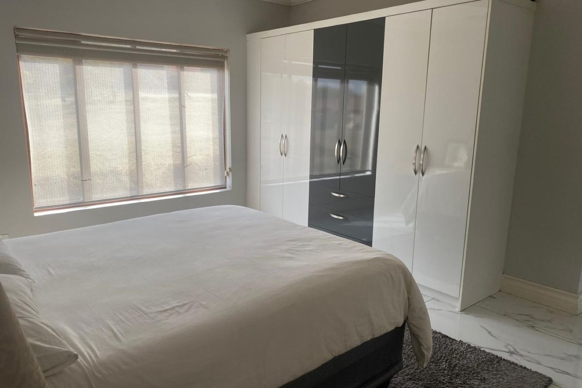 A well-maintained bedroom featuring modern high-gloss built-in cupboards, marble-look floor tiles, and neutral wall finishes.