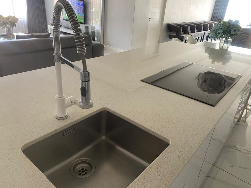 Modern open-plan kitchen featuring a large island with quartz countertops, integrated induction cooktop, undermount sink, and high-end gooseneck faucet.
