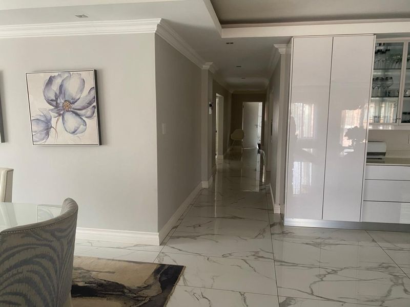 A bright, modern hallway featuring polished marble-look floor tiles, recessed lighting, and sleek built-in cabinetry, leading towards the private living quarters.