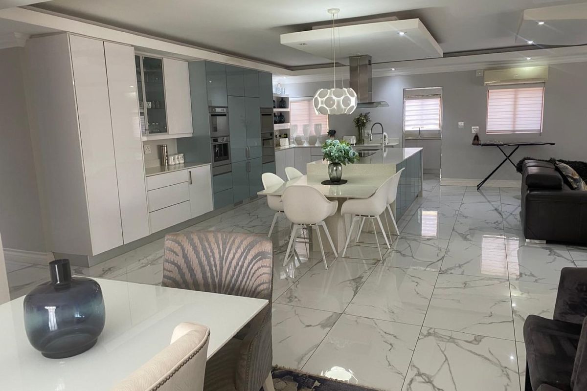 Modern open-plan kitchen and dining area featuring high-gloss cabinetry, a central island, and polished marble-look floor tiles with recessed ceiling lighting.