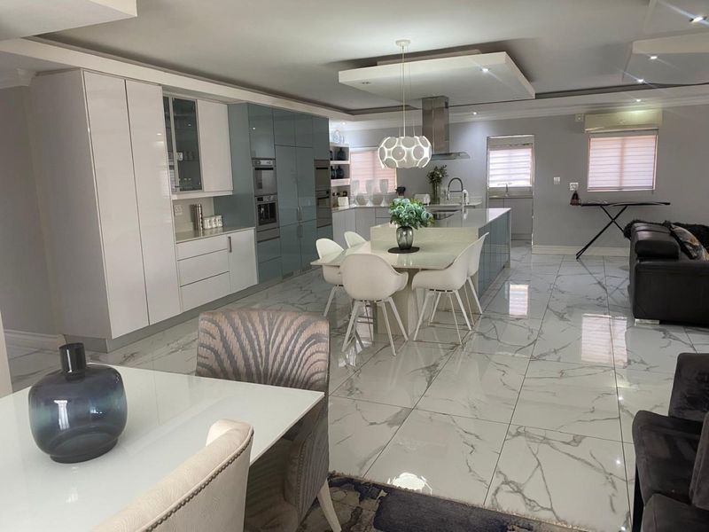 Modern open-plan kitchen and dining area featuring high-gloss cabinetry, a central island, and polished marble-look floor tiles with recessed ceiling lighting.
