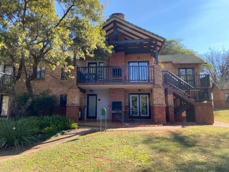 Rear view of a double-story brick house featuring a balcony, external staircase, and a built-in braai area overlooking the garden.
