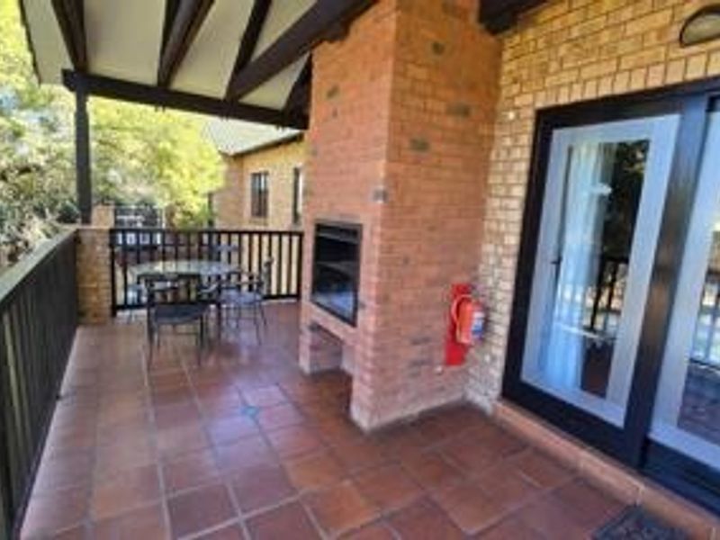 A covered balcony featuring tiled flooring, exposed timber beams, and a built-in brick braai, providing an ideal space for outdoor entertaining.