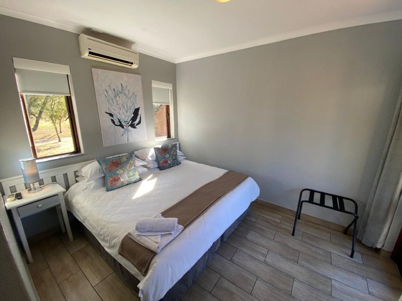 A well-maintained bedroom featuring tiled flooring, a wall-mounted split-system air conditioner, and dual windows with roller blinds.