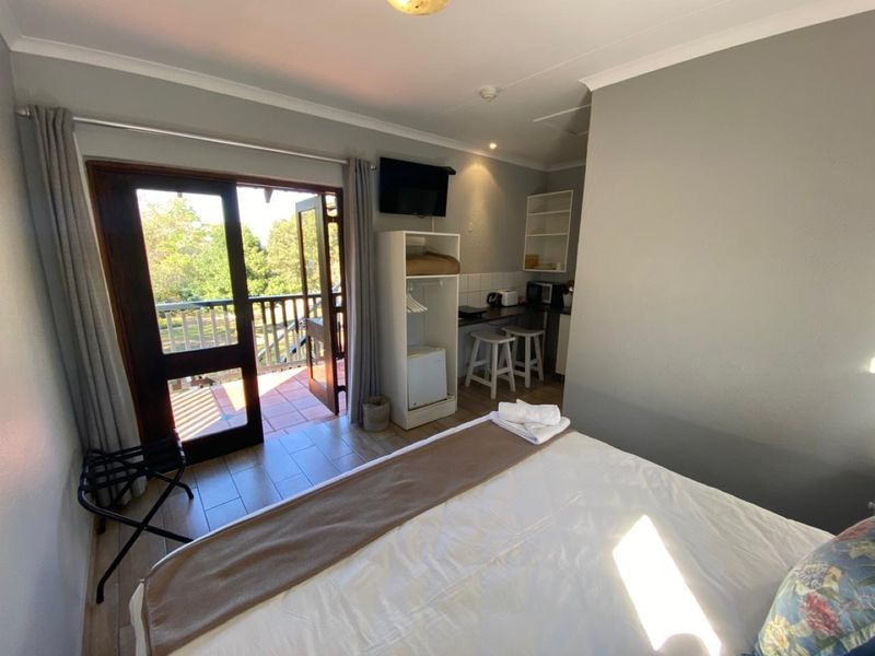 A bedroom featuring tiled flooring, a small built-in kitchenette area, and direct access to an outdoor balcony through a glass sliding door.