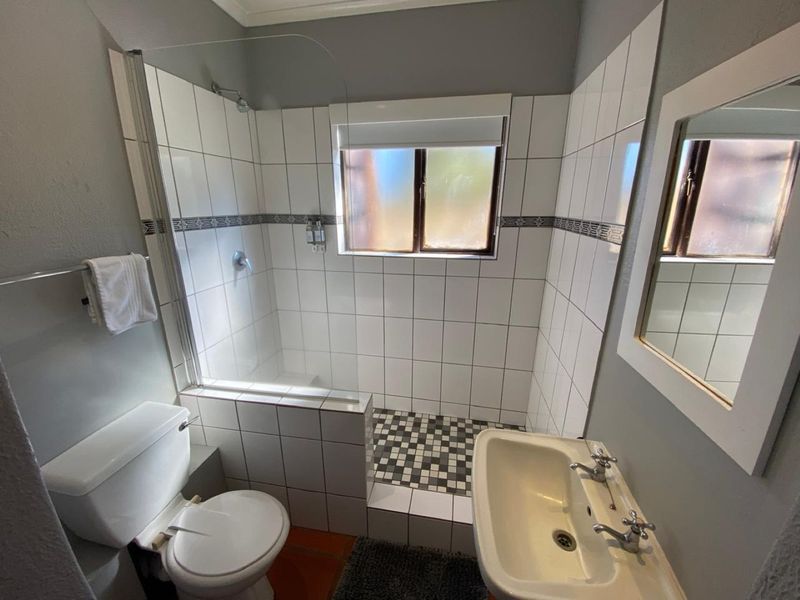 A functional bathroom featuring a walk-in shower with glass screen, pedestal basin, and tiled finishes throughout.