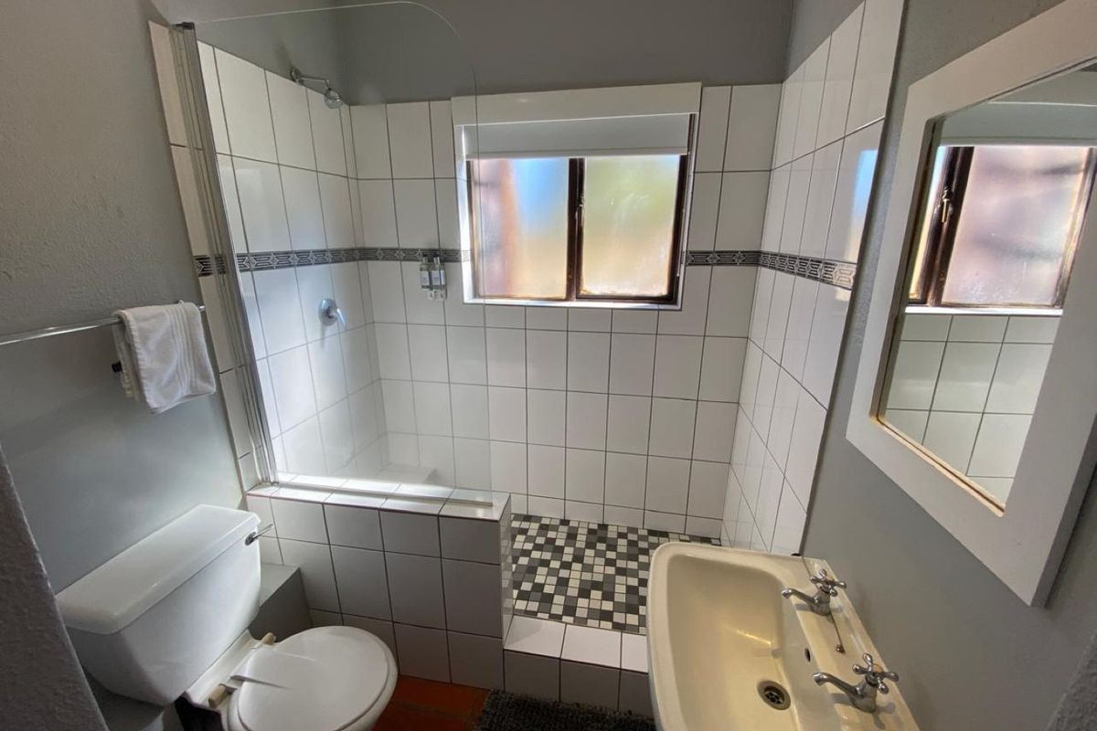 A functional bathroom featuring a walk-in shower with glass screen, pedestal basin, and tiled finishes throughout.