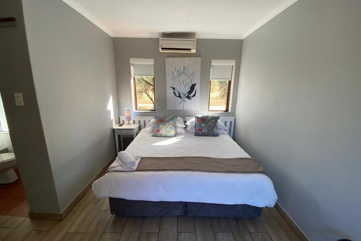 A well-maintained bedroom featuring tiled flooring, a wall-mounted split-system air conditioner, and dual windows with roller blinds.