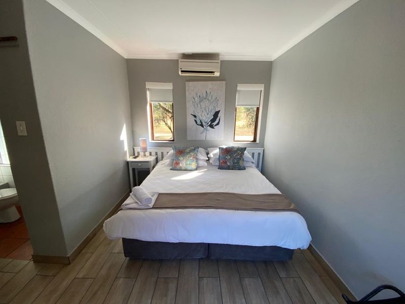 A well-maintained bedroom featuring tiled flooring, a wall-mounted split-system air conditioner, and dual windows with roller blinds.
