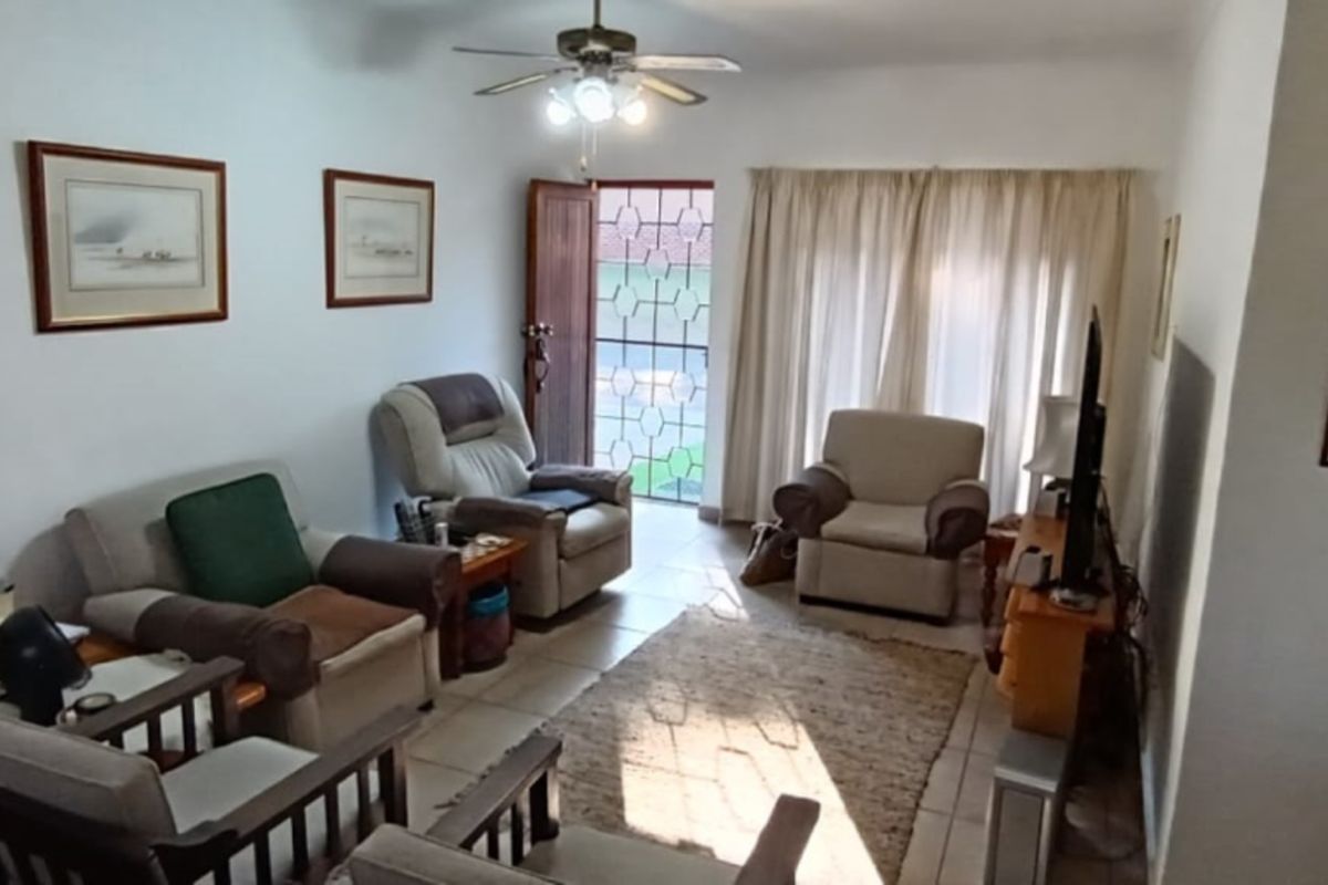 A living room featuring tiled flooring, a ceiling fan, and a security gate leading to the exterior.