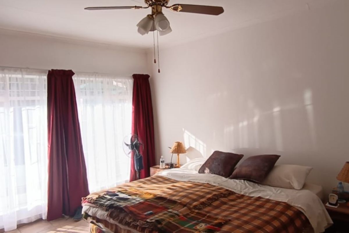 A bedroom featuring tiled flooring and a ceiling fan, with large windows allowing for natural light.