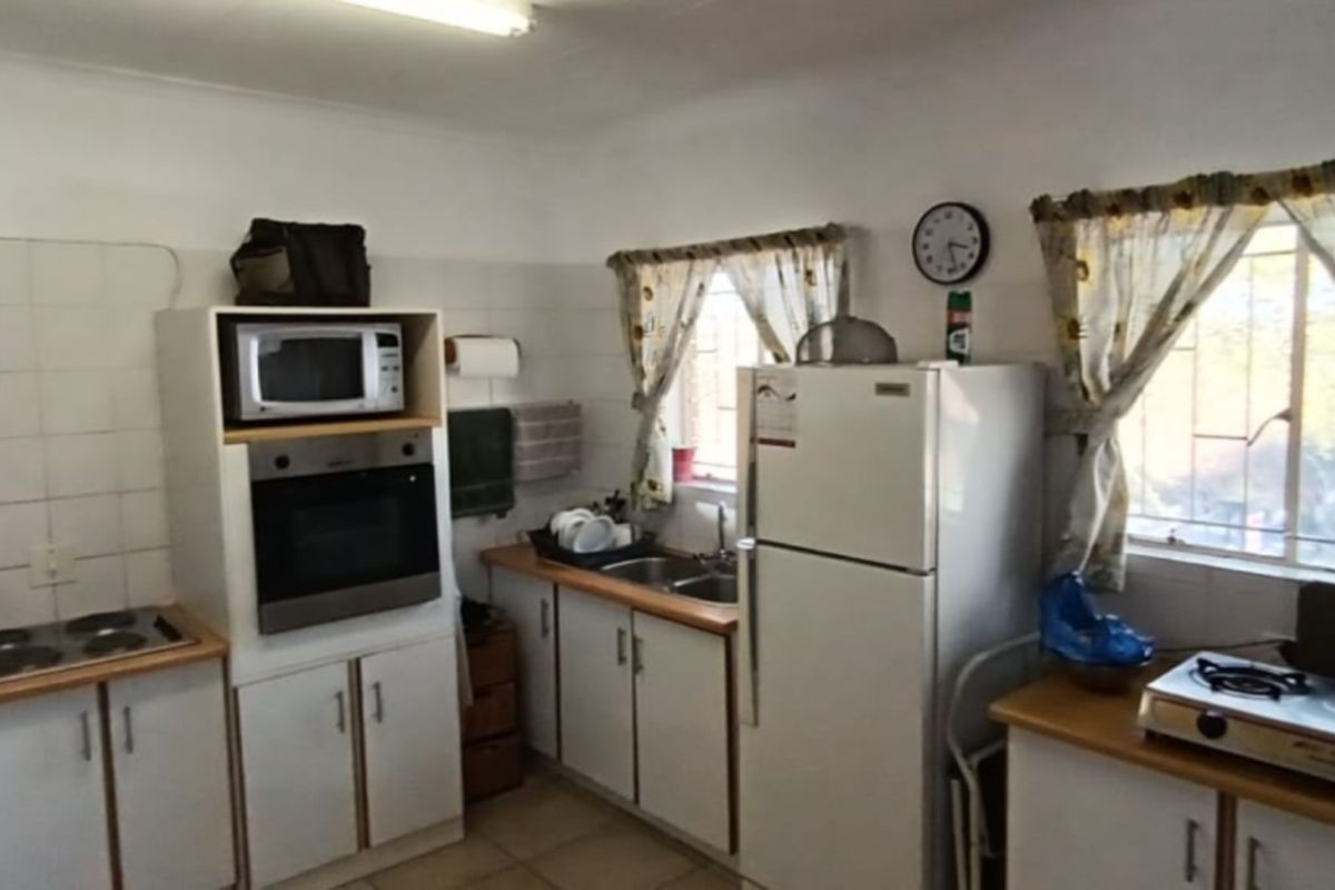A functional kitchen featuring built-in oven, microwave, electric hob, double sink, and ample cabinetry with tiled splashbacks and security bars on the windows.