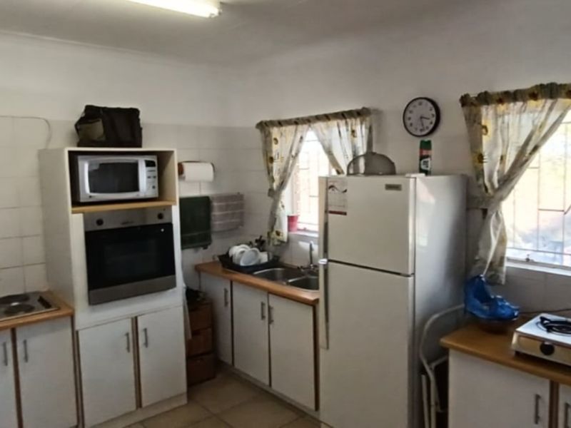 A functional kitchen featuring built-in oven, microwave, electric hob, double sink, and ample cabinetry with tiled splashbacks and security bars on the windows.