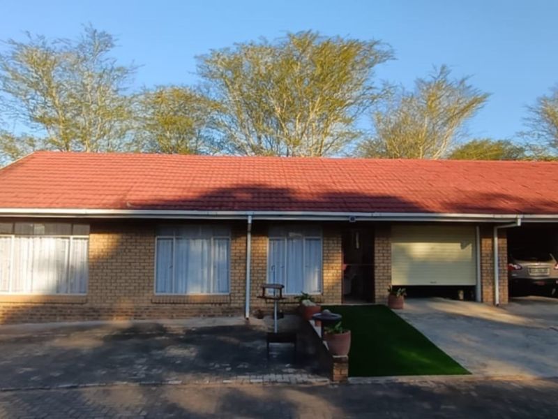 Front elevation of a duet property featuring a brick facade, tiled roof, and integrated garage with a paved driveway.