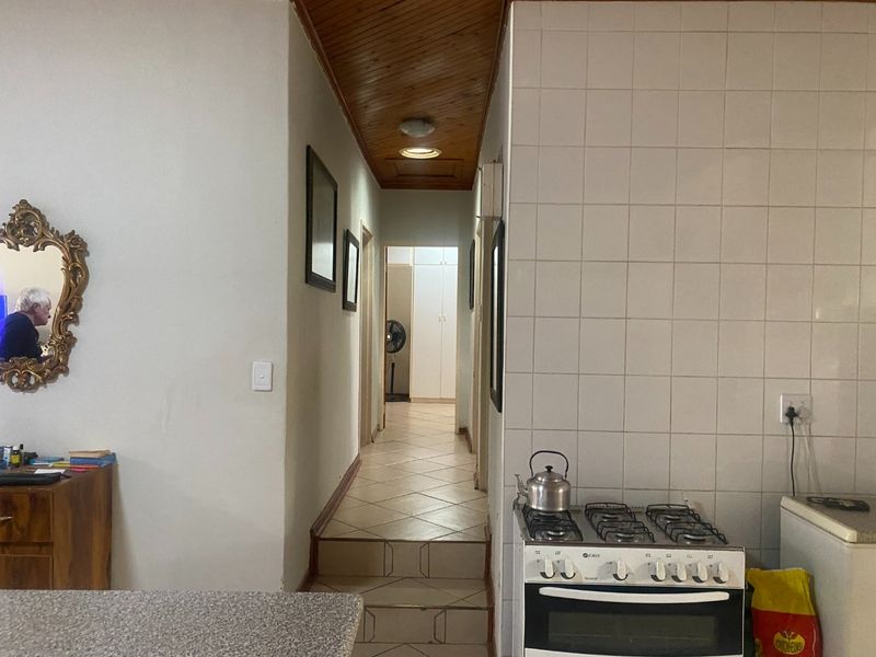 Kitchen area featuring a gas stove, tiled splashback, and tiled flooring, leading into a hallway with a timber-paneled ceiling.