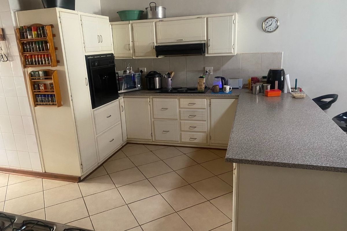 Functional kitchen featuring built-in cabinetry, oven, hob, extractor fan, and a breakfast bar with tiled flooring and backsplash.