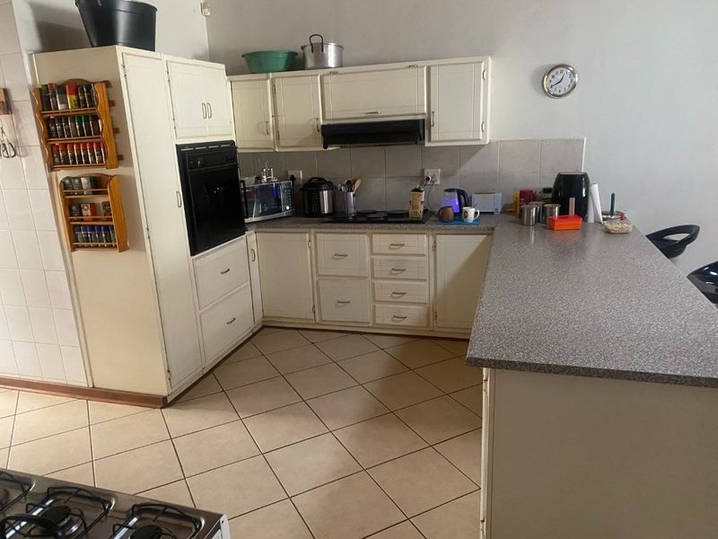 Functional kitchen featuring built-in cabinetry, oven, hob, extractor fan, and a breakfast bar with tiled flooring and backsplash.
