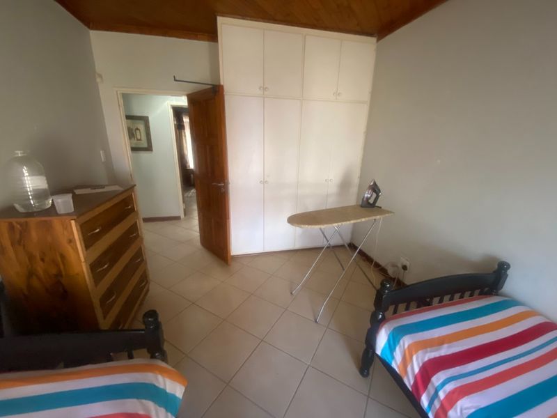 A bedroom featuring tiled flooring, built-in cupboards, and a timber ceiling, offering a functional space with potential for modernization.