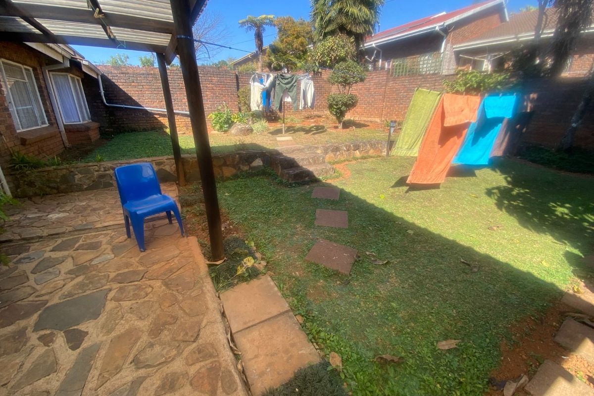 A rear garden area featuring a stone-paved patio, a covered outdoor structure, and a brick-walled perimeter with a lawn.