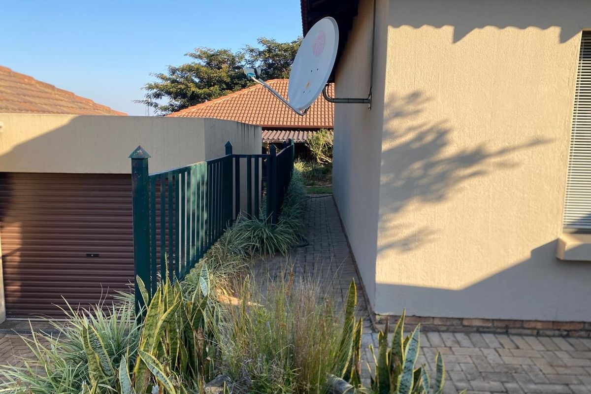 A side exterior view of the property featuring a paved walkway, metal fencing, and a satellite dish mounted on the exterior wall.