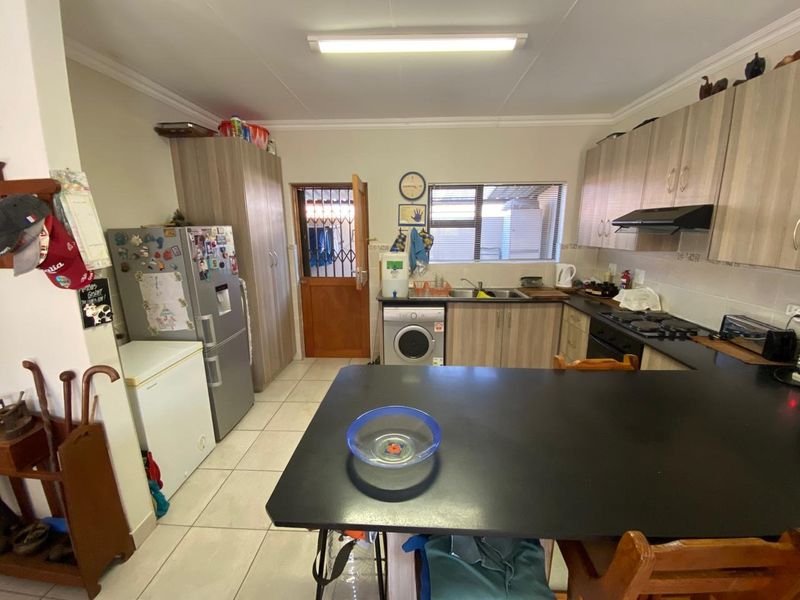 Functional kitchen featuring wood-look cabinetry, dark countertops, integrated appliances, and tiled flooring with direct access to an exterior security door.