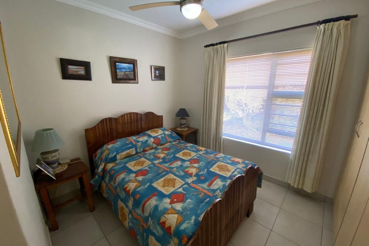 A functional bedroom featuring tiled flooring, a ceiling fan, and a built-in wardrobe, offering a comfortable and practical living space.