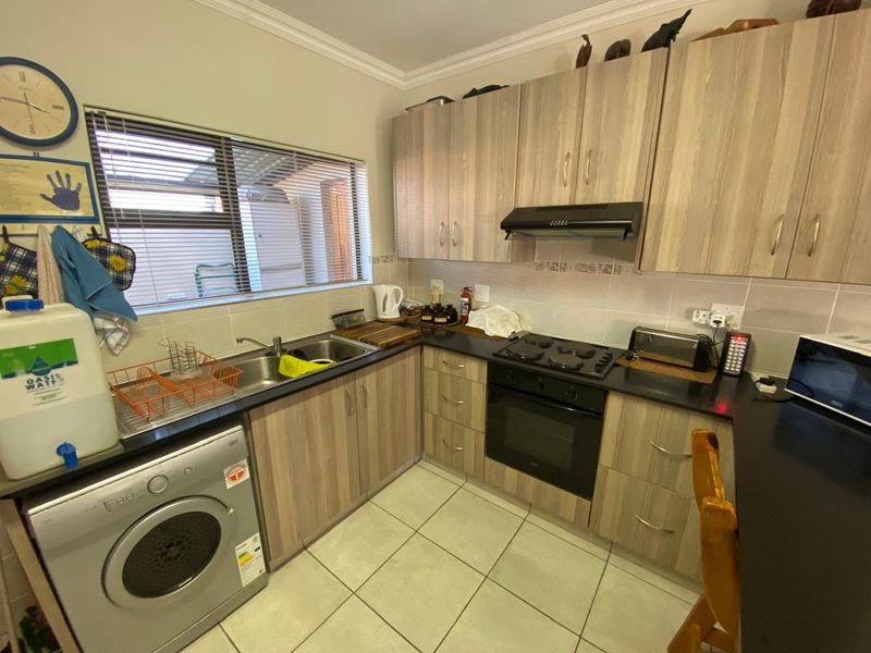 Functional kitchen featuring light wood-tone cabinetry, black countertops, integrated oven and hob, and tiled flooring with a window overlooking the exterior.