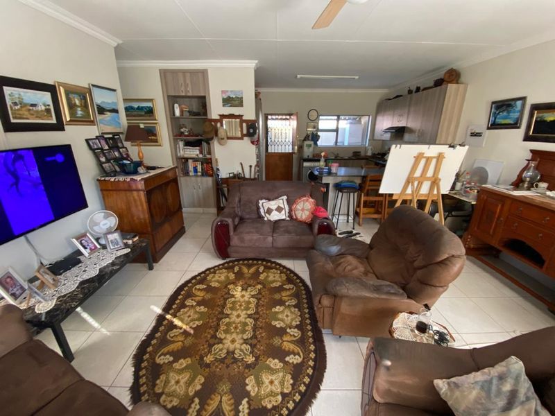 Open-plan living area featuring tiled flooring, a ceiling fan, and a functional kitchen with built-in cabinetry and an island.