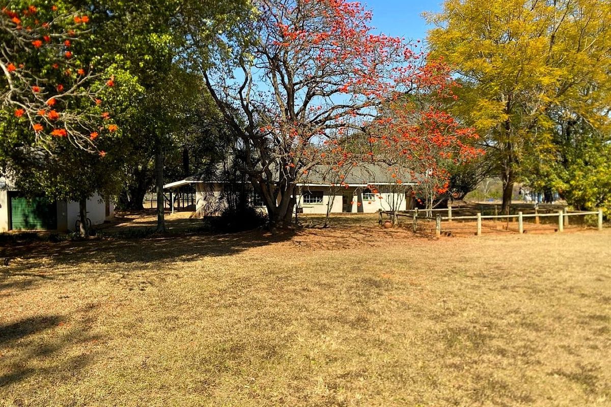 A view of the rear exterior of the property featuring a spacious garden, mature trees, and a covered patio area.