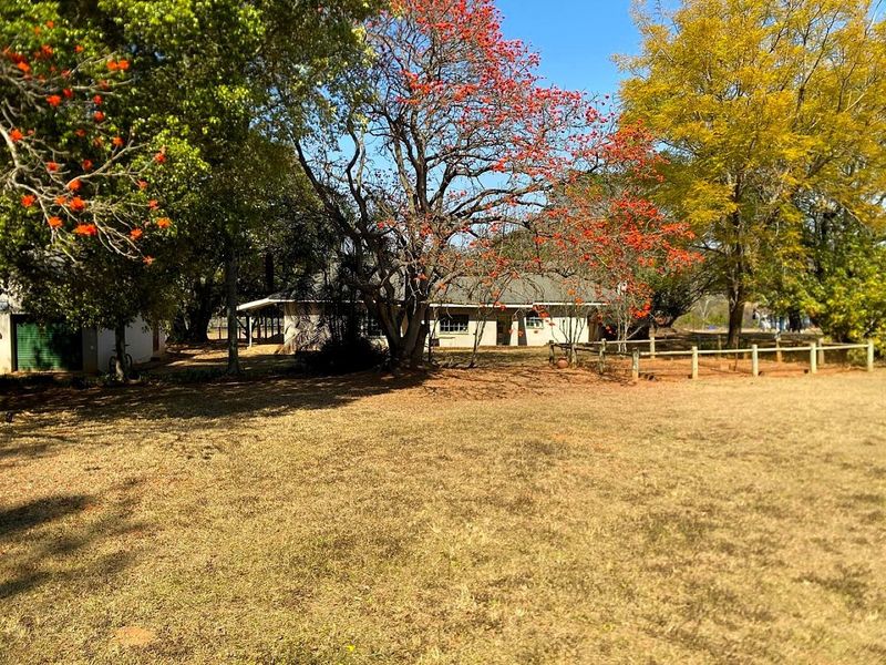 A view of the rear exterior of the property featuring a spacious garden, mature trees, and a covered patio area.