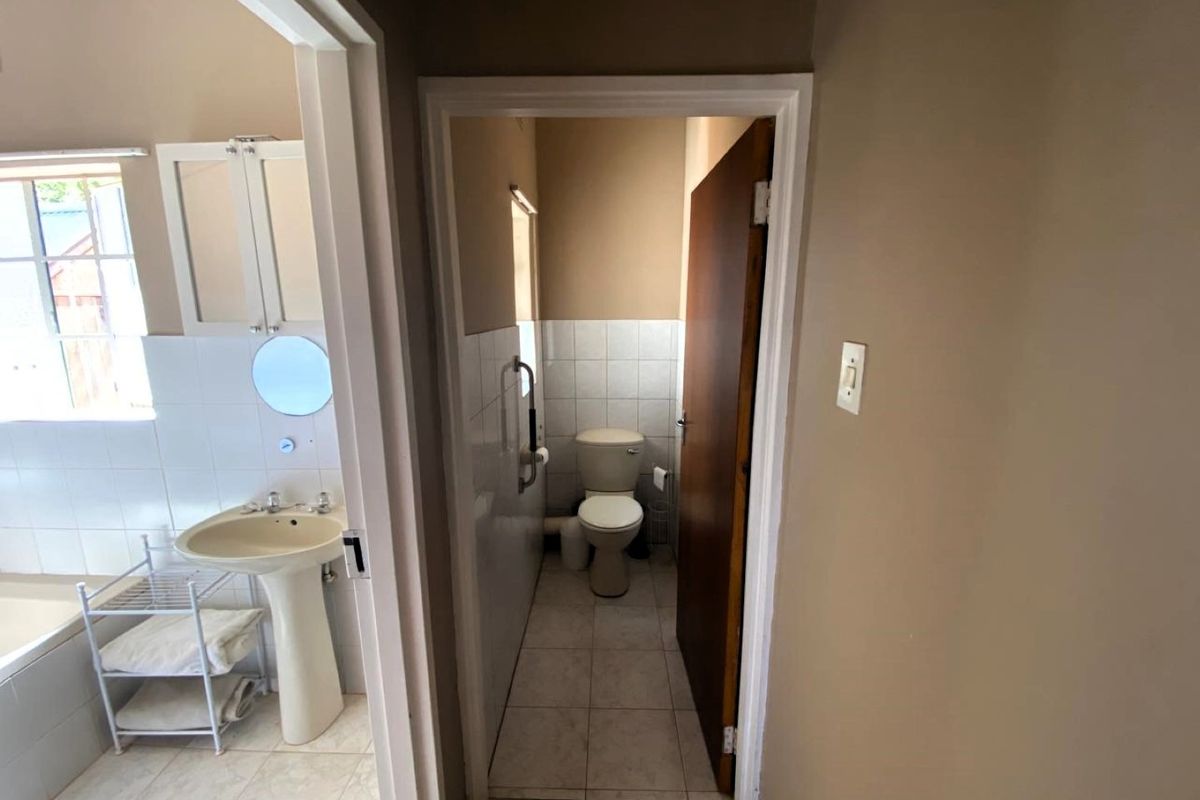A functional bathroom featuring a pedestal basin and a separate toilet area with tiled finishes and a safety grab rail.