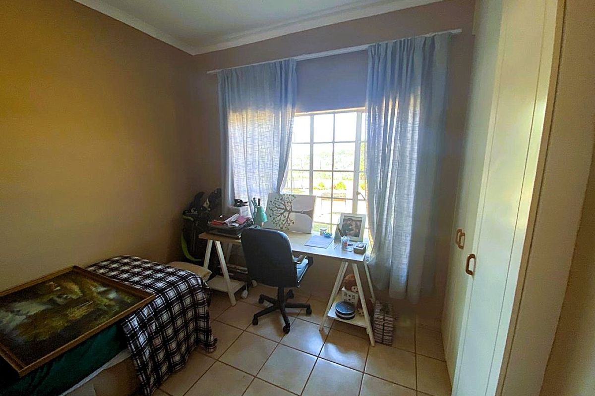 A functional bedroom featuring tiled flooring, built-in cupboards, and a window with security bars, providing a practical space for rest or study.