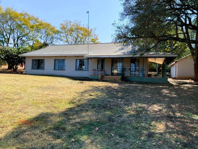 Rear view of a single-story small holding residence featuring a corrugated metal roof, covered patio area, and established garden surroundings.