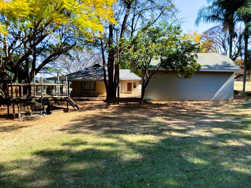 A view of the rear garden area featuring mature trees, a wooden deck structure, and the rear elevation of the main dwelling.