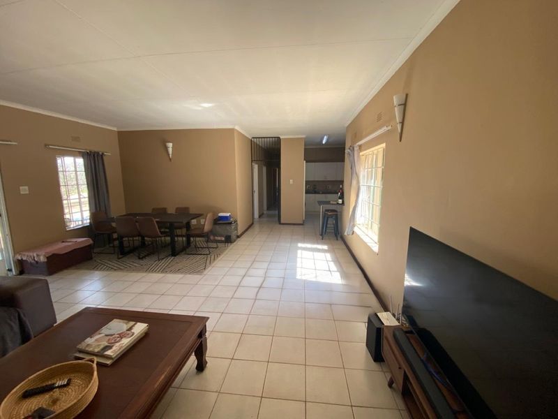 Spacious open-plan living and dining area featuring tiled flooring, neutral wall tones, and a functional kitchen space with a breakfast counter.