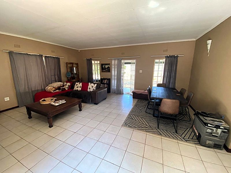Spacious open-plan living and dining area featuring neutral tiled flooring, coved ceilings, and direct access to the outdoor patio through a glass-paneled door.