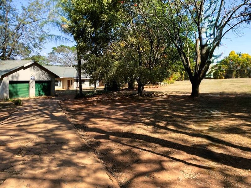 Front view of the small holding featuring a paved driveway leading to a double garage with roller shutter doors and established garden trees.