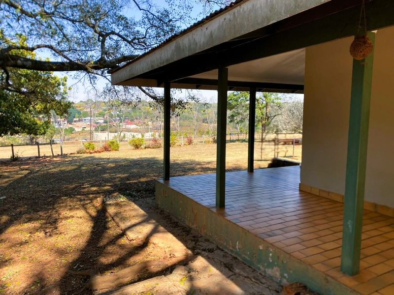 A covered outdoor patio area with tiled flooring and support pillars, overlooking the surrounding garden and landscape.