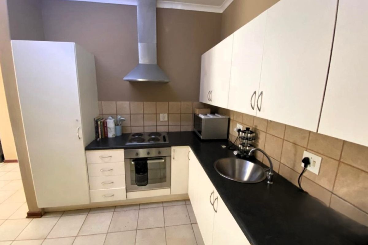 A functional kitchen featuring white cabinetry, dark countertops, a stainless steel sink, and integrated cooking appliances with a tiled backsplash.