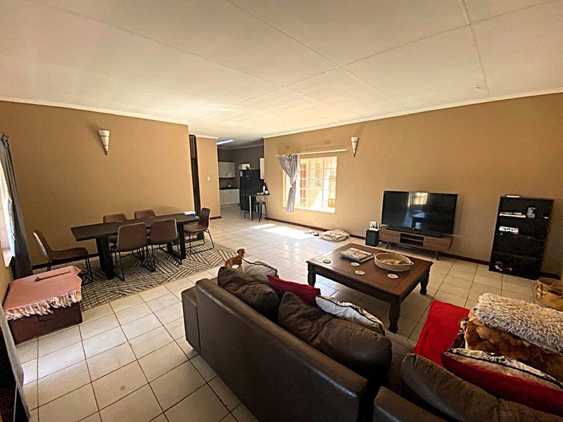Spacious open-plan living and dining area featuring tiled flooring and neutral wall tones, with a view through to the kitchen area.