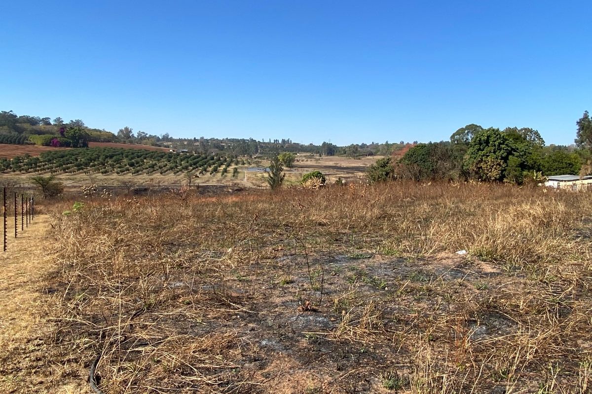 A wide-angle view of a vacant residential plot featuring dry, scorched vegetation and perimeter electric fencing, overlooking a rural landscape.