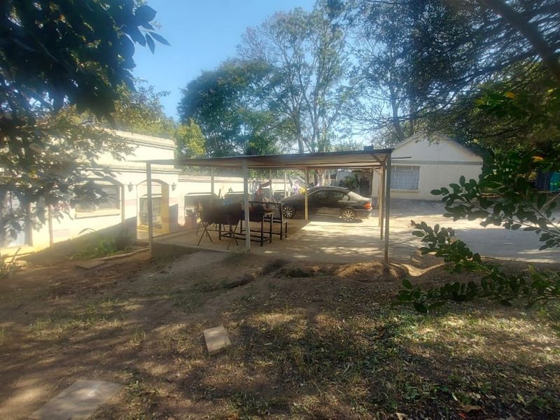 Rear exterior view of the small holding featuring a covered patio area and concrete driveway space surrounded by mature trees.