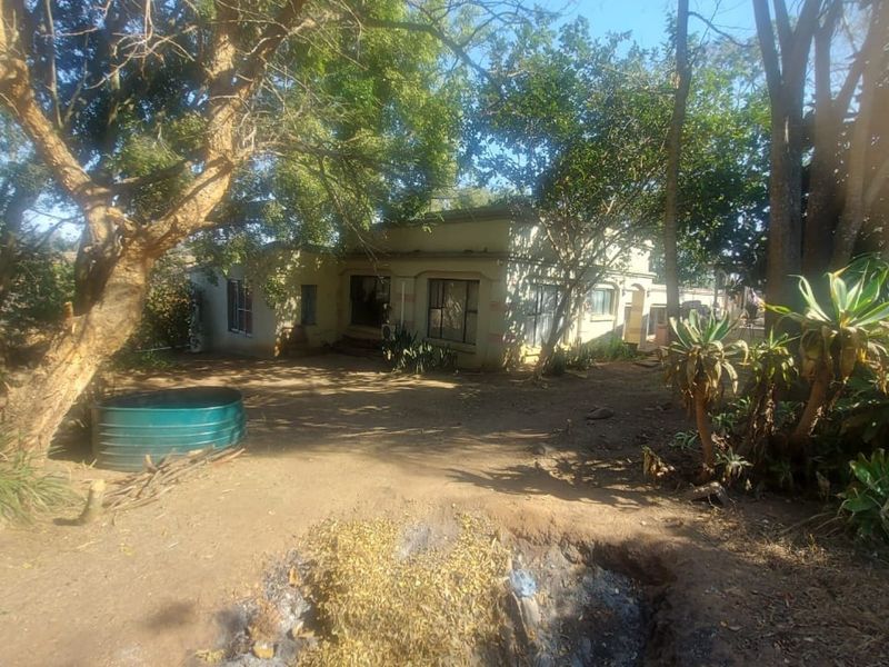 Rear view of the property showing a single-story dwelling set within a large, wooded garden area with a metal water tank.