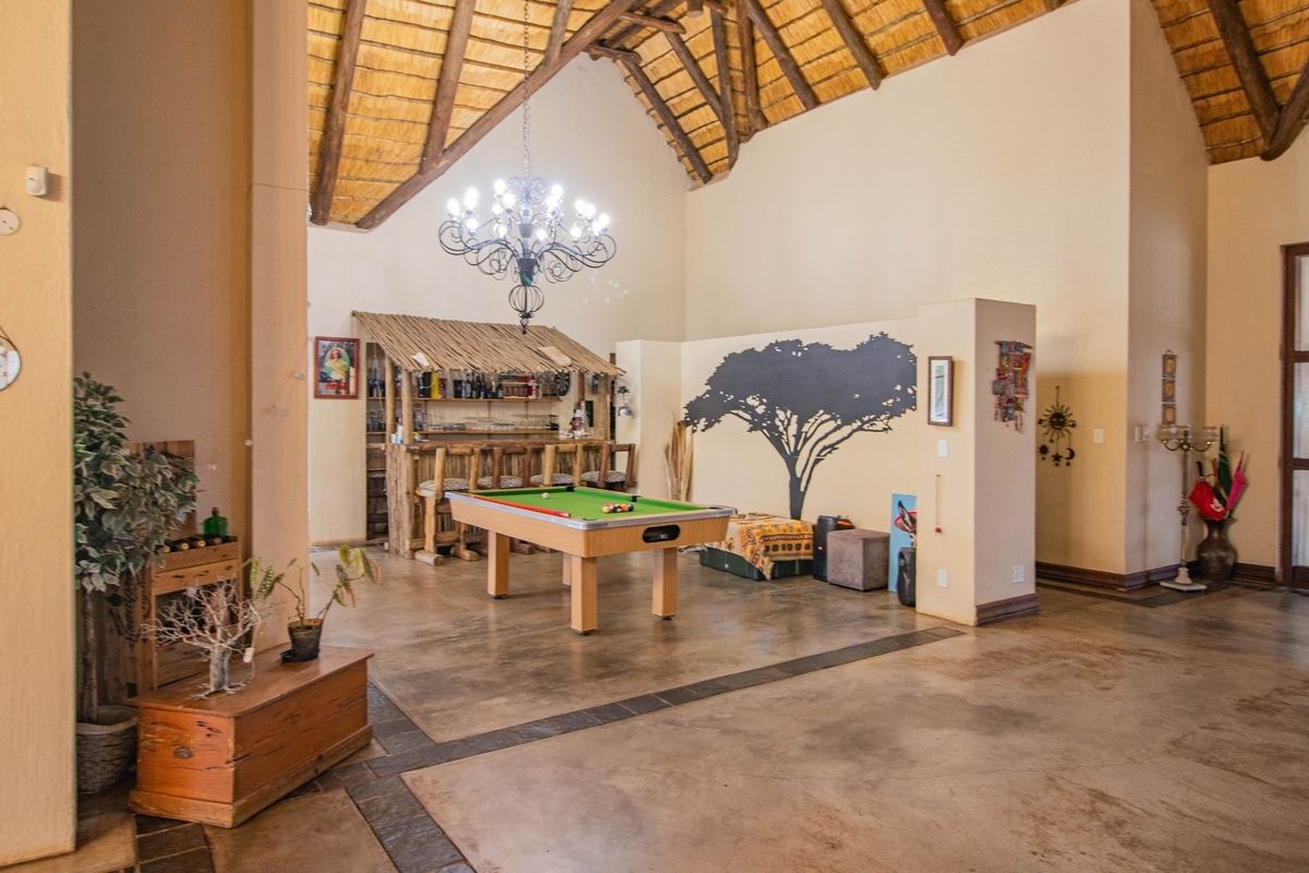 Spacious living area featuring a high double-volume thatched roof with exposed timber trusses and polished concrete flooring, including a built-in bar area.